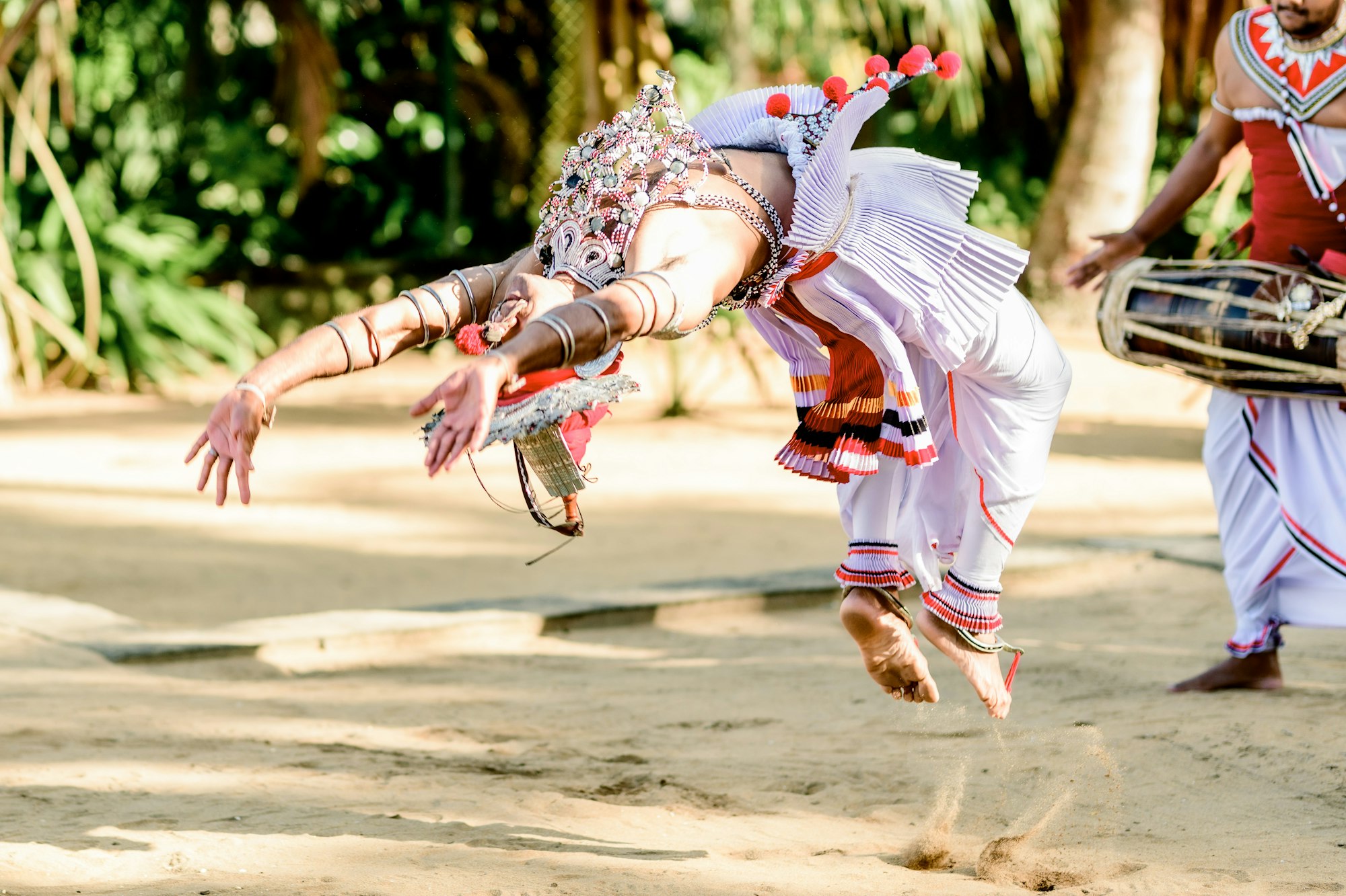 A traditional Sri Lankan dancer in mid-leap beside a drummer
