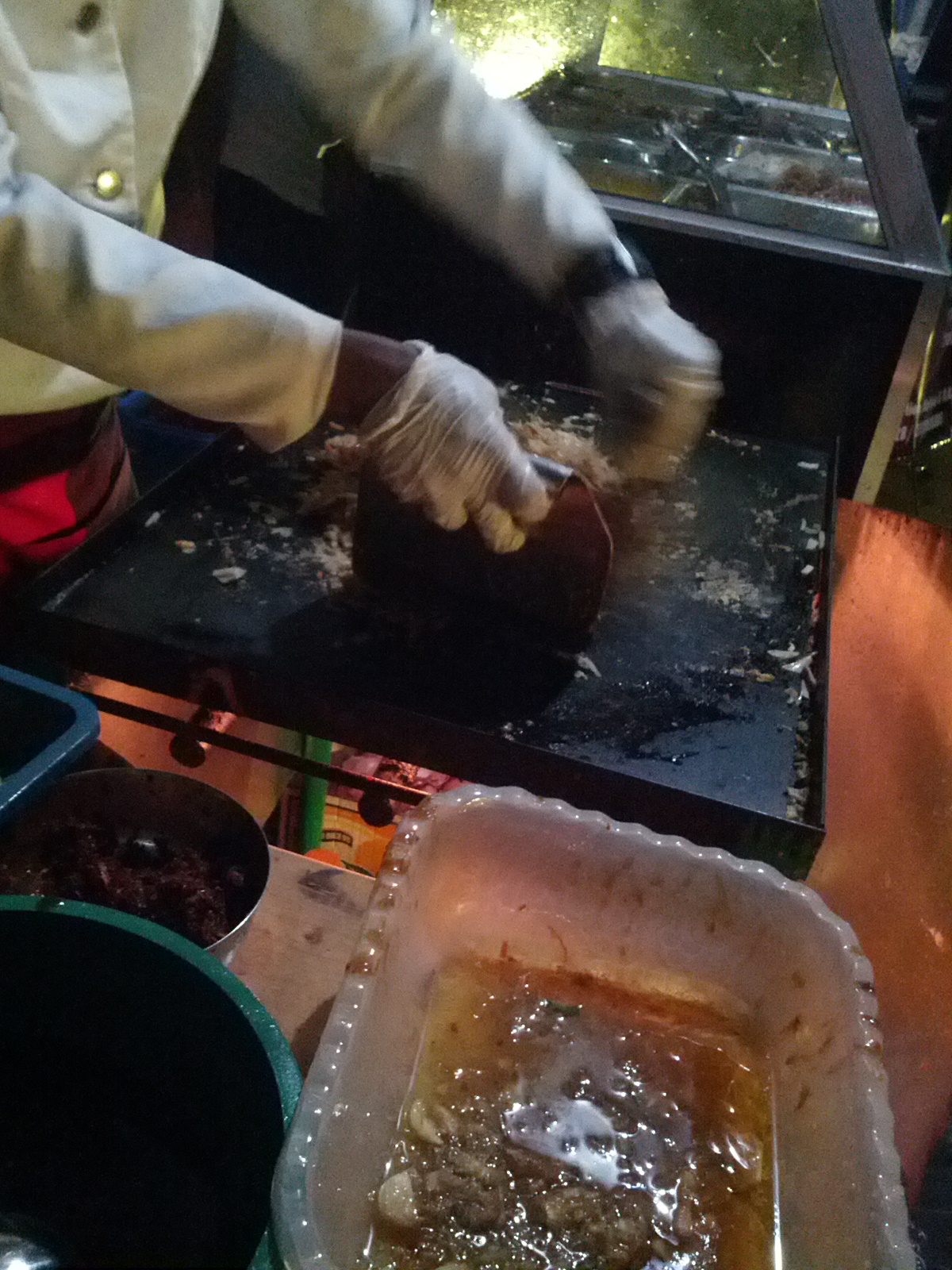 A cook chopping kottu roti with twin blades on a hot steel plate.